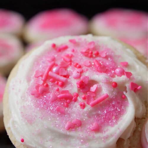 A close up of a sugar cookie with white frosting and pink candy sprinkles on it.