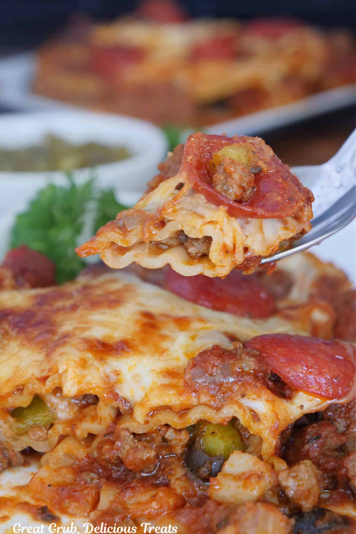 A fork with a bite on supreme pizza stuffed manicotti on it held above a plate with a serving of the pasta on it.