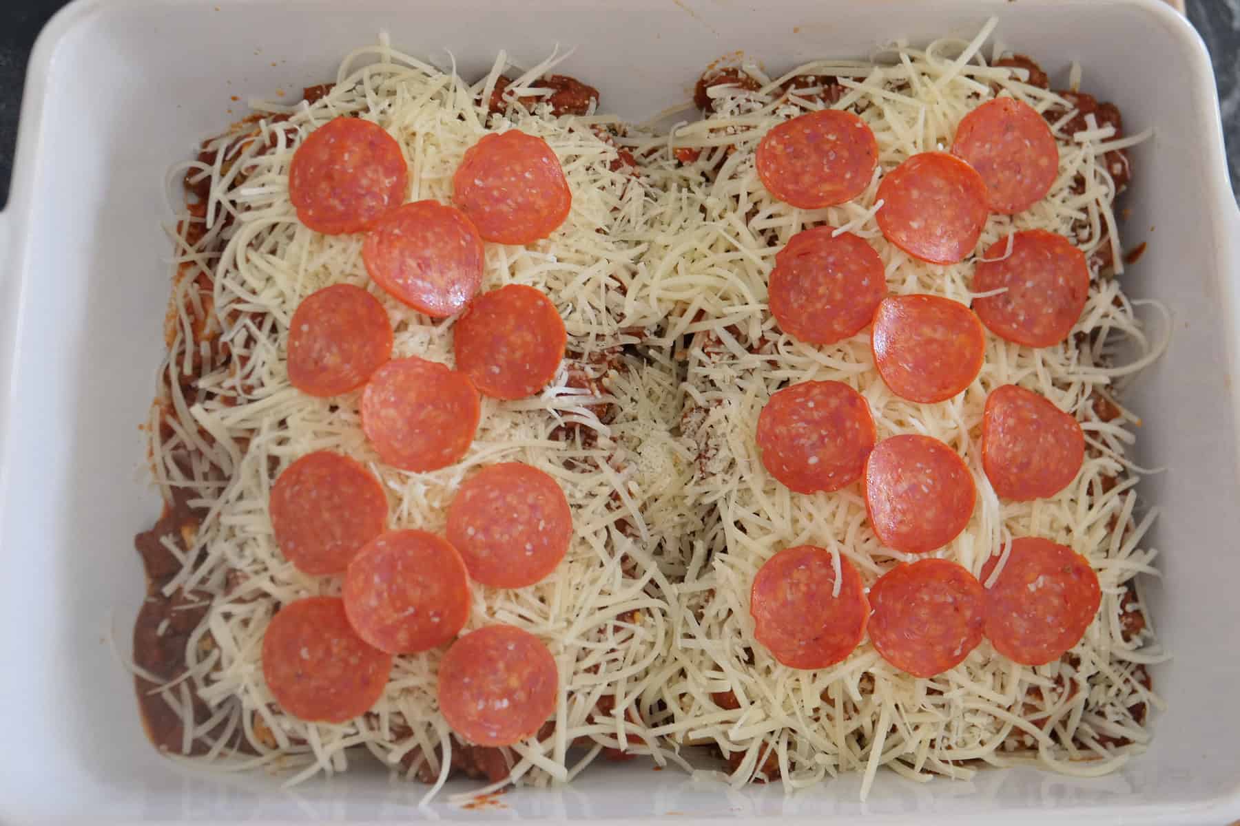 A white baking dish with the stuffed manicotti noodles covered with cheese and pepperoni slices on top.