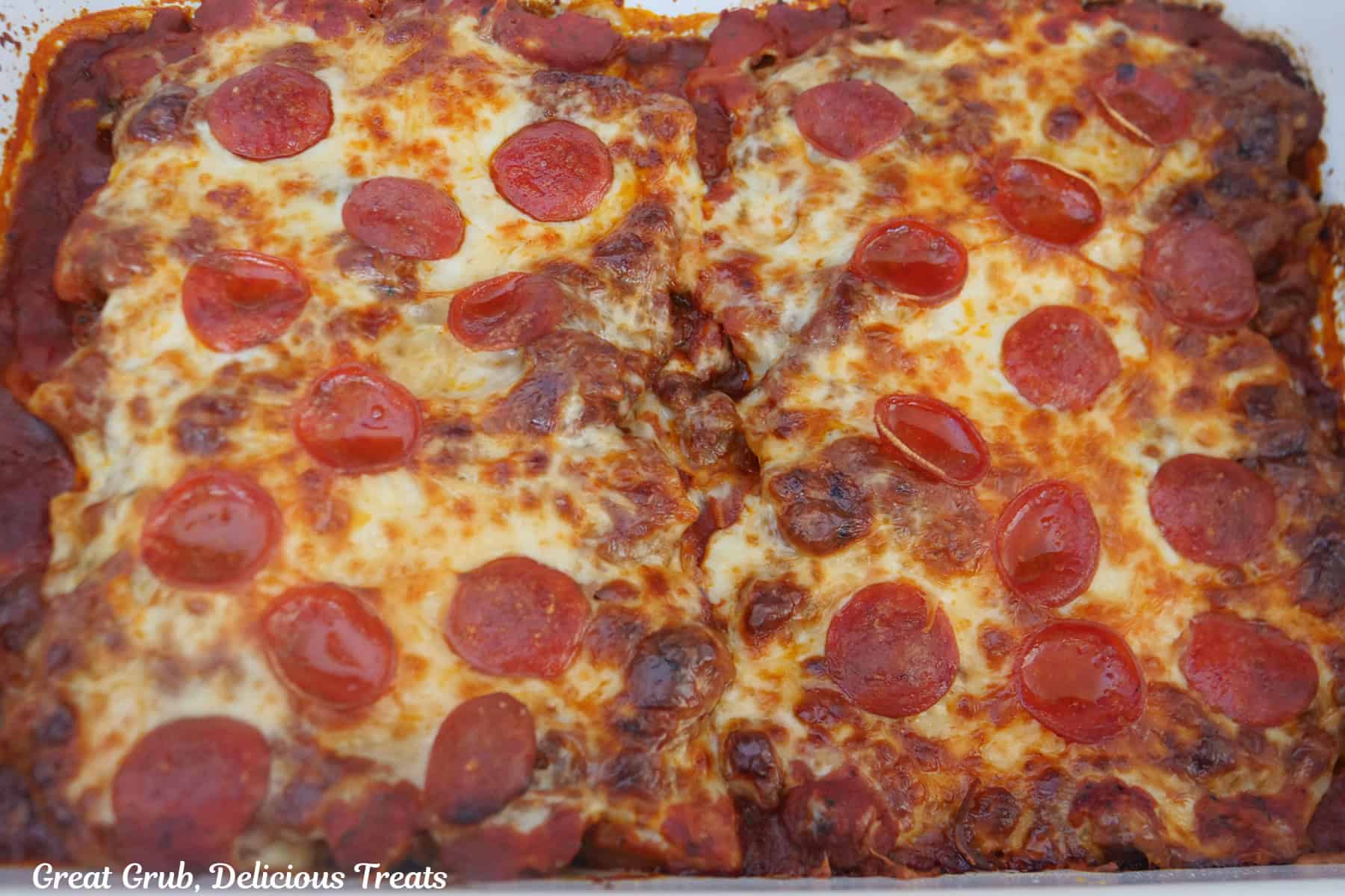 A white baking dish with baked supreme pizza stuffed manicotti .