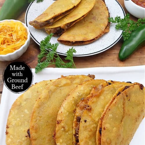 Five tacos lined on a white plate with a small plate in the background.