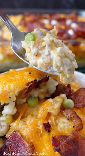 A bite of tater tot casserole on a spoon hovering over a bowl of it.