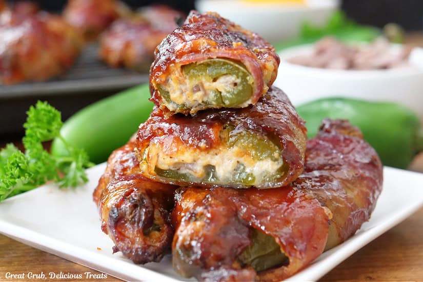 A horizontal photo of a small white square plate with 4 bacon wrapped stuffed jalapenos.