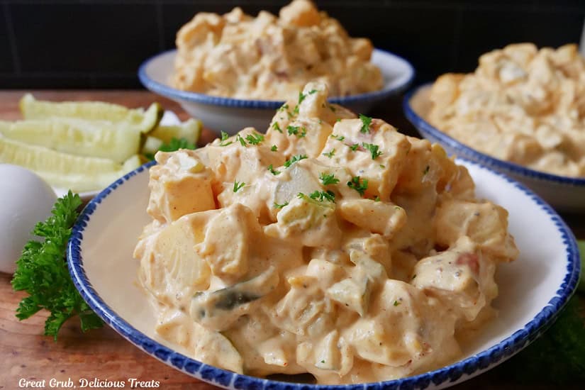 Three white bowls with blue trim filled with potato salad.