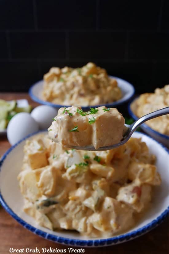A spoonful of potato salad held over a bowl filled with a serving of potato salad.