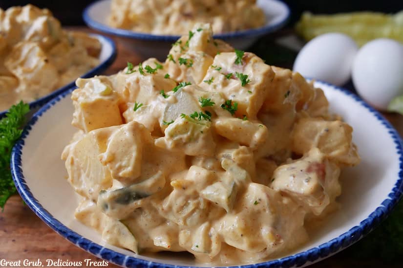 An oval white bowl with blue trim filled with potato salad.