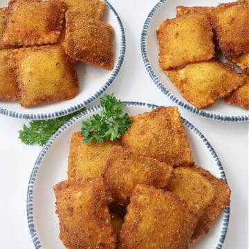 Three white plates with blue trim with toasted raviolis on them.