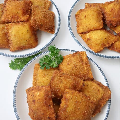 Three white plates with blue trim with toasted raviolis on them.