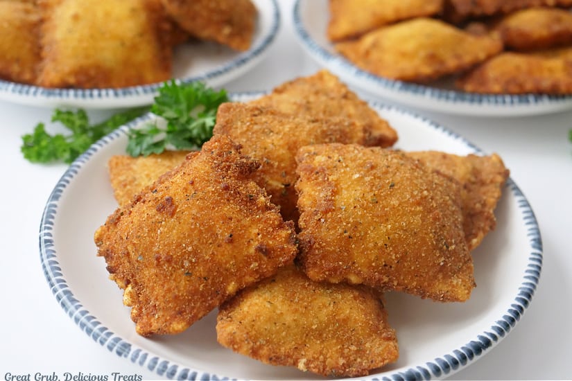 A horizontal photo of white plates with blue trim with a small stack of toasted raviolis on them.