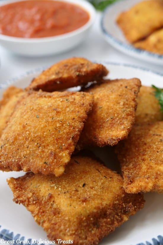 A salad size white plate with blue trim with a stack of toasted raviolis on it.