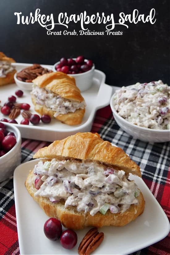 A red and black plaid surface with white plates with croissants filled with turkey cranberry salad.