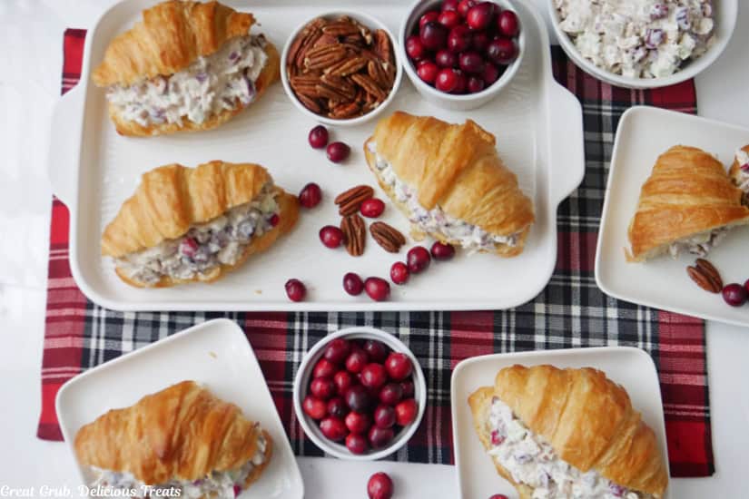 A white, red and black plaid surface with white plates and a white tray filled with croissant turkey cranberry salad sandwiches.
