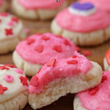 A few bite-size sugar cookies with pink and white buttercream frosting and candy sprinkles on top, and one with a bite taken out of it.