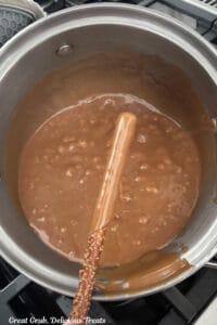 A saucepan with homemade caramel in it and a pretzel rod being dipped half way up in the caramel.