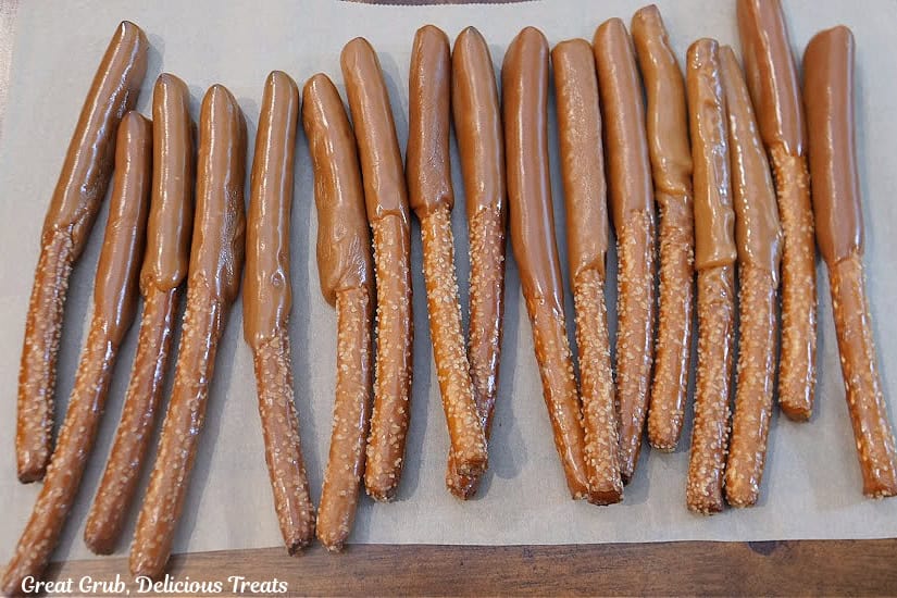 Seventeen pretzel rods covered half way up in caramel placed on parchment paper.