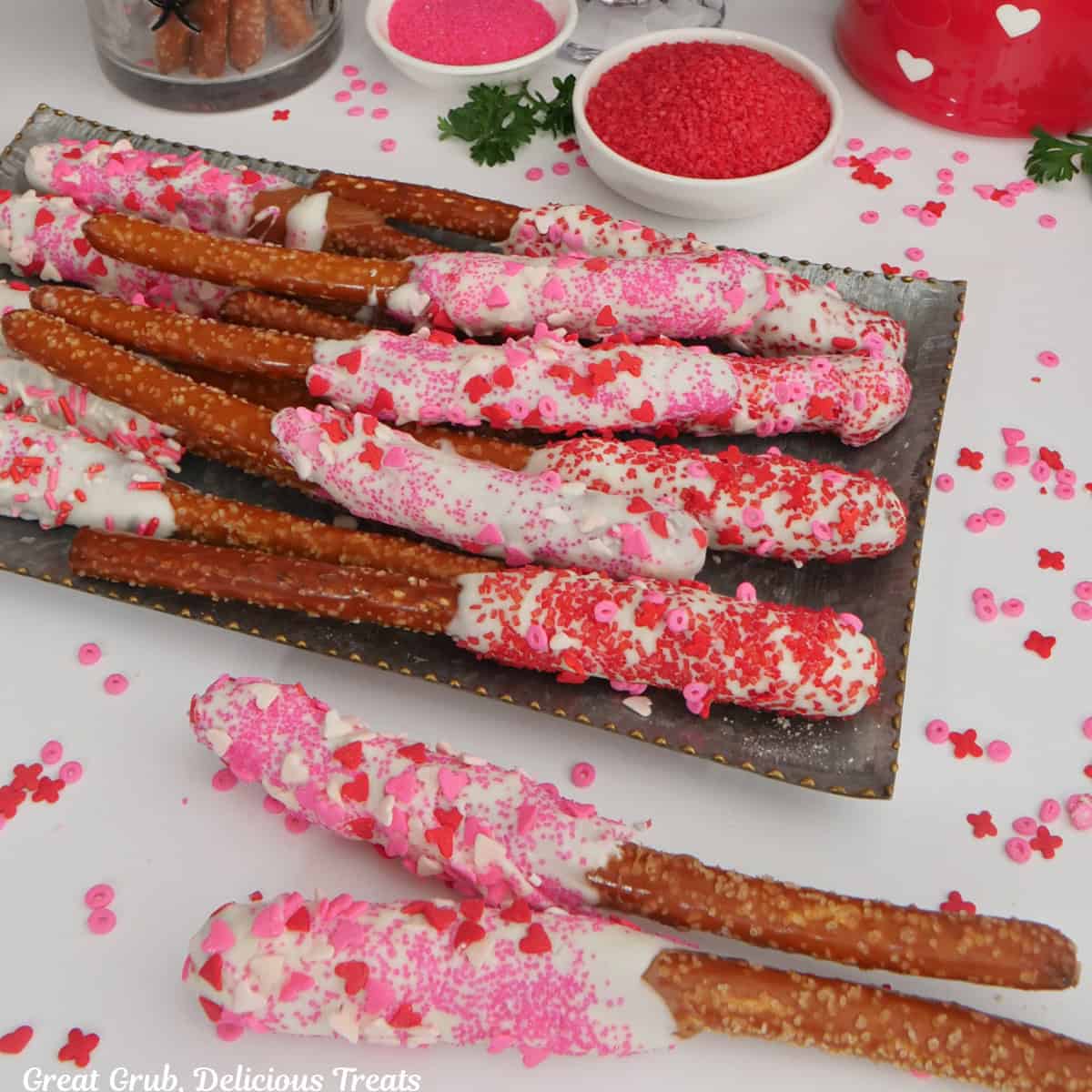 A white surface with pretzel rods decorated with a Valentine theme dessert.