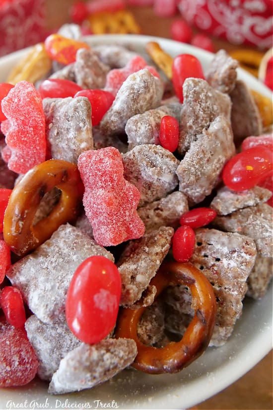 Valentine Puppy Chow Mix is a sweet and spicy muddy buddy mix made with cinnamon candies, chex cereal, chocolate, peanut butter, and pretzels. A super close up photo of Valentine Puppy Chow Mix. in a white bowl.