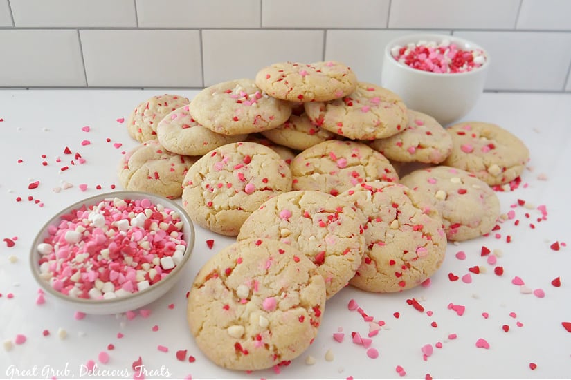 Valentine Sugar Cookies are soft, chewy cookies that are loaded with Valentine’s Day sprinkles. A horizontal picture of Valentine's Day sugar cookies stacked in a pile with sprinkles spread around the cookies.