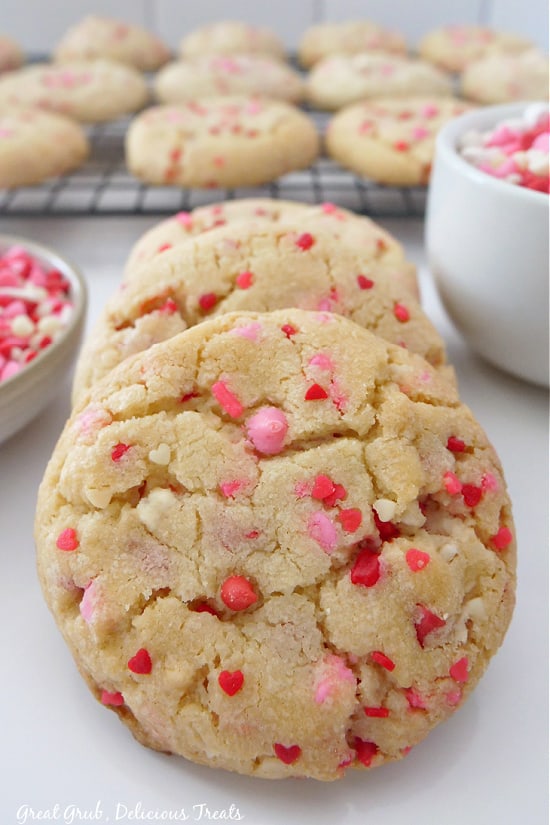 Valentine Sugar Cookies are deliciously soft and chewy sugar cookies that are loaded with sprinkles. A close-up picture of sugars cookies lined up one behind the other with more cookies in the background.