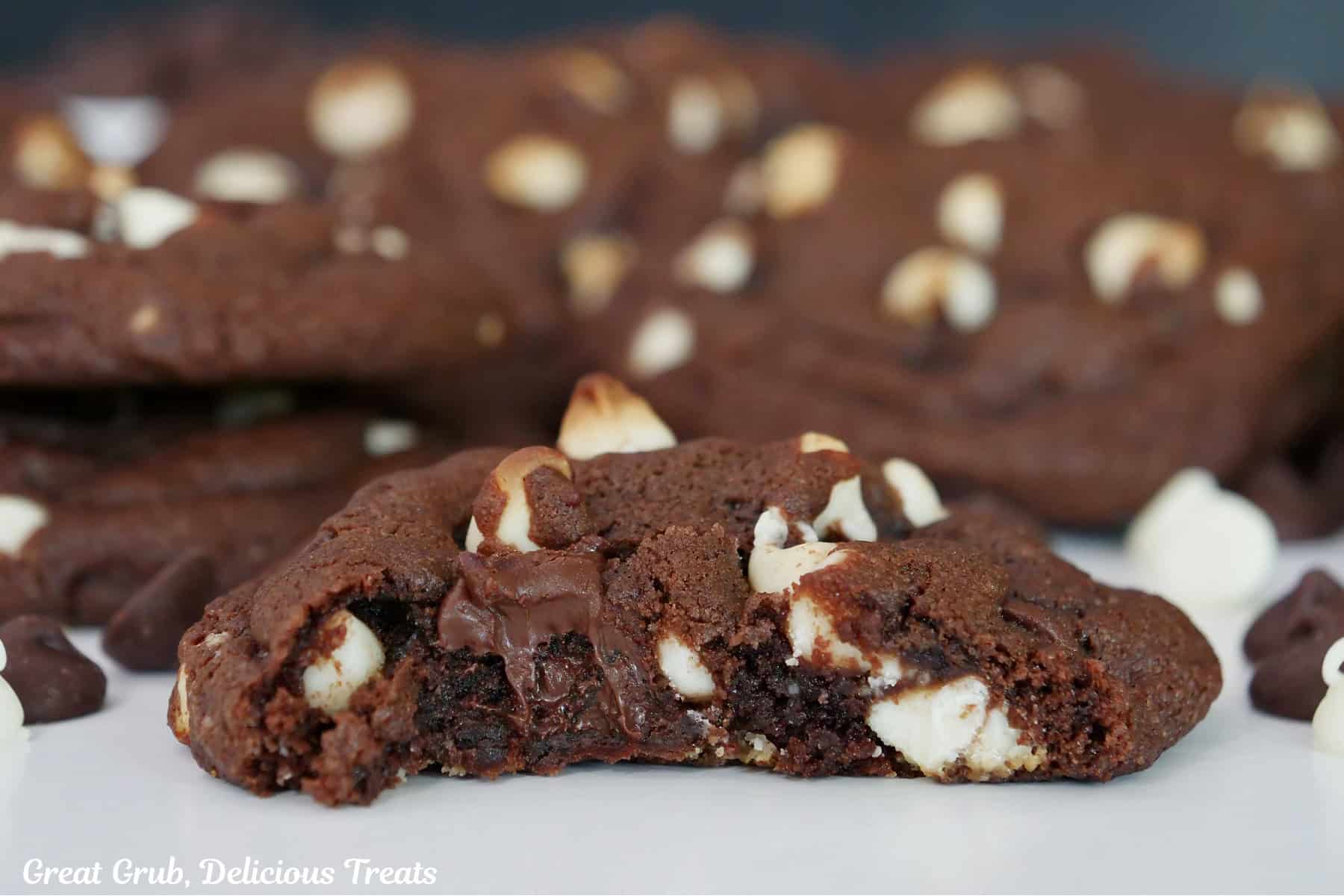 A white surface with a couple dozen cookies on it with a bite taken out of the cookie in front.