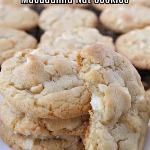 White chocolate macadamia nut cookies stacked on a white plate with a wire rack filled with cookies sits in the background.